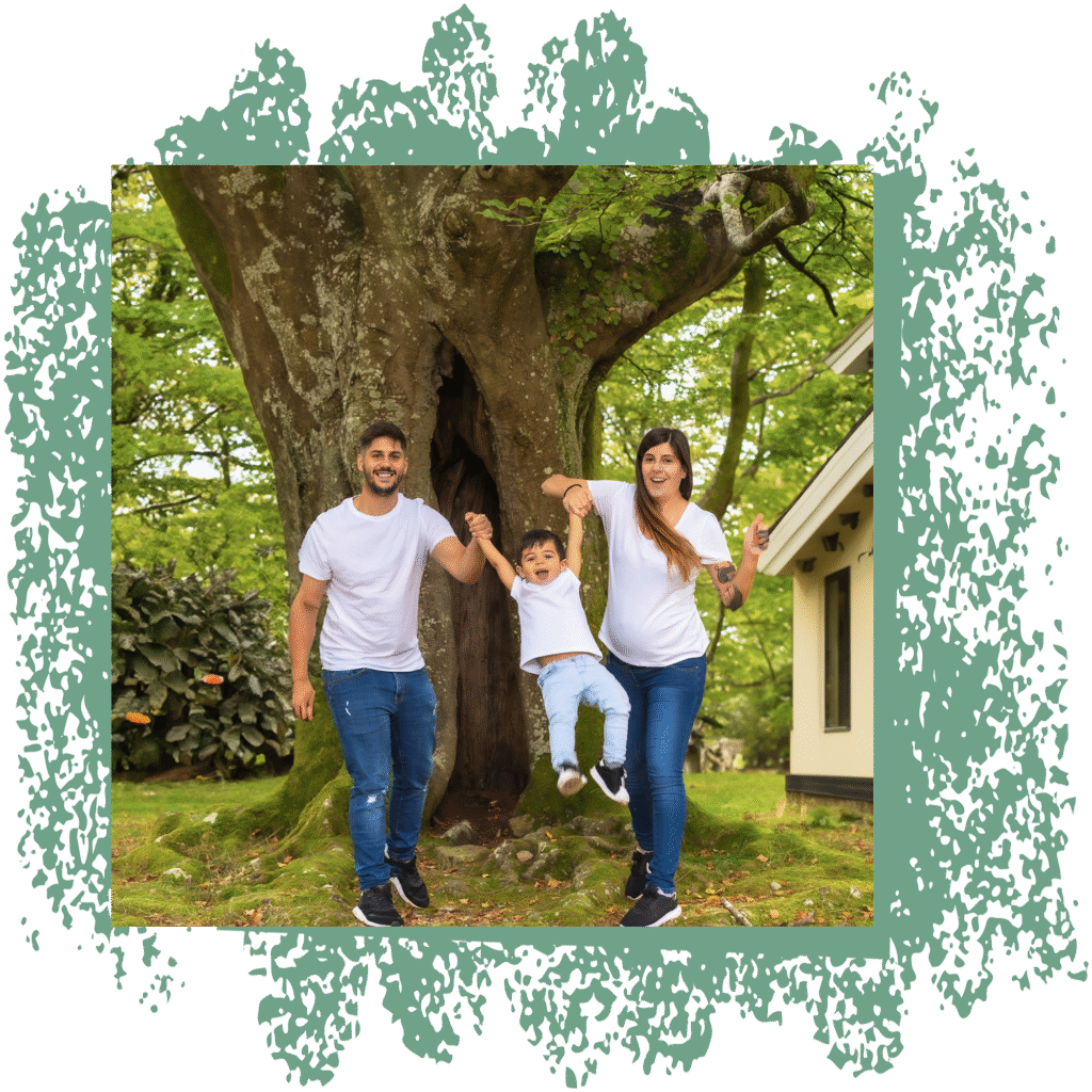 Famille souriante devant un grand arbre dans un jardin, représentant un foyer particulier avec un arbre imposant à proximité de la maison